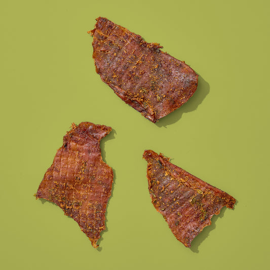Three pieces of ginger scallion calamari jerky on a green background